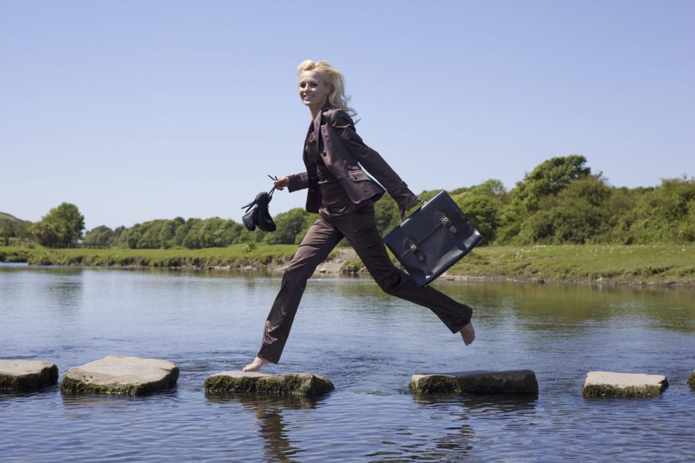 A woman wearing a grey business suit stepping across the water on stones